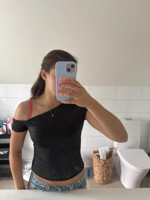 Svart oneshoulder topp - Säljer en svart oneshoulder topp med tight passform. Toppen är ribbad och har kort ärm på ena sidan medan andra axeln är bar. Perfekt för dig som vill ha en trendig och enkel look till jeans eller kjol