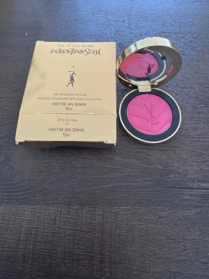 YSL rosa puderrouge i guldförpackning - Säljer ett lyxigt puderrouge från Yves Saint Laurent i en snygg guldfärgad dosa med spegel. Rouget har en intensiv rosa nyans och är pressat med YSL-loggan. Perfekt för att ge kinderna en fräsch färg och glow.