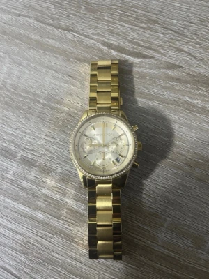 Guldig klocka från Michael Kors - Snygg guldig klocka från Michael Kors med länkarmband i metall och rund urtavla. Klockan har flera små urtavlor och detaljer runt boetten som ger en lyxig känsla. Perfekt accessoar för dig som vill sticka ut med stil.