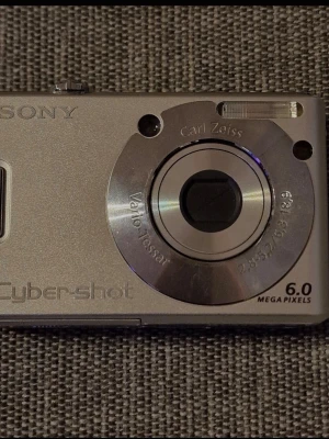 Sony Cyber-shot DSC-W30 digitalkamera - Snygg silverfärgad Sony Cyber-shot DSC-W30 med Carl Zeiss Vario-Tessar-objektiv och 6.0 megapixlar. Kameran har en kompakt, rektangulär design med stor display på baksidan och tydliga knappar för enkel navigering. Perfekt för dig som gillar retro digitala kameror.