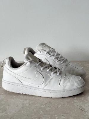 Nike Court Borough Low | EU 37,5  - Säljer ett par klassiska vita Nike sneakers i lågt modell. Skorna är tillverkade i slätt läder med matchande vita skosnören och sula. Ikoniska swoosh-loggan på sidan och perforerade detaljer vid tån för extra stilpoäng.