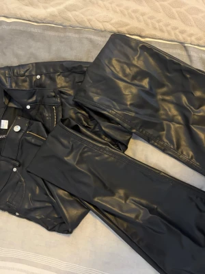 Svarta coated jeans från Hm - Säljer ett par svarta coated jeans från Gina Tricot med glansig finish. Byxorna har klassisk femficksmodell, silverfärgade knappar och dragkedja. Materialet är stretchigt och ger en cool läderlook som passar perfekt till streetwear eller en edgy outfit.