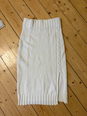 Vit stickad kjol från Lindex - Säljer en jättefin vit stickad midikjol från Lindex. Kjolen har bred ribbad midja, ribbade kanter och en snygg slits framtill med flätad detalj längs sidan.
