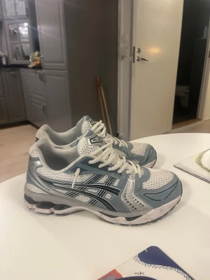 Asics gel kayano 14 vit och turkosa  - Säljer ett par fräscha Asics sneakers i vitt och turkos med klassiska svarta stripes på sidan. Skorna har mesh- och syntetmaterial för bra andningsförmåga och komfort. Perfekta för dig som gillar sportig stil och vill ha något bekvämt till vardags.
