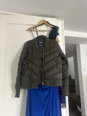 Olivgrön pufferjacka från Svea - Säljer en olivgrön pufferjacka från Svea med coolt chevronmönster i vadderingen. Jackan har ribbade muddar, hög krage och dragkedja framtill. Perfekt för kalla dagar och riktigt snygg till streetwear-stilen.
