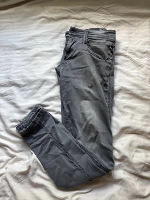 Grå  jeans från Replay - Säljer ett par grå jeans från Replay med klassisk femficksdesign och dragkedjegylf. Jeansen har en snygg tvättad look och smala ben som sitter tajt hela vägen ner. Perfekta för dig som gillar en modern och avslappnad stil.
