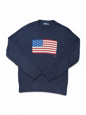 Mörkblå stickad tröja Polo Ralph Lauren - Mörkblå stickad tröja från Polo Ralph Lauren med amerikansk flagga i rött, vitt och blått på bröstet. Rund halsringning och ribbstickade muddar vid ärmslut och nederkant. RL-broderi i rött vid flaggan. Perfekt för dig som gillar klassisk college-stil.