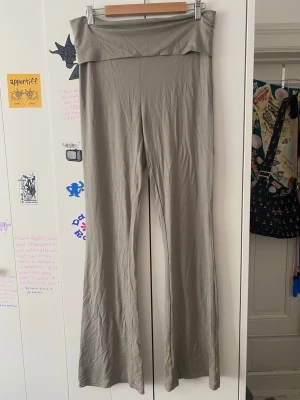 Beiga bootcut leggings med hög midja - Säljer ett par beiga leggings med bootcut och extra hög midja som kan vikas ner. De är i mjukt stretchigt material och har en enkel, stilren look utan synliga loggor eller detaljer. Perfekta för en avslappnad och trendig stil.