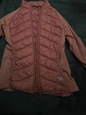 Rosa quiltad cardiganjacka - Snygg rosa cardiganjacka med quiltade partier framtill och dragkedja. Jackan har en hög krage och är tillverkad i ett mjukt material med släta ärmar. Perfekt för lager på lager och har en sportig look med diskret logga på nedre sidan.