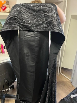 Svart glittrig sjal med paljetter - Den här klänningen är i ett mycket kraftigt material och är i mycket gott skick. Den är ganska lång och har draperingar med silvermönster på sig. Den har ärmar som också är fulla av silvermönster. Den användes bara en gång på ett bröllop och är i mycket gott skick, inga tecken på slitage! Köpte den från ett Instagramkonto @lerich.se. Jag köpte den för 3500 kr plus frakt.