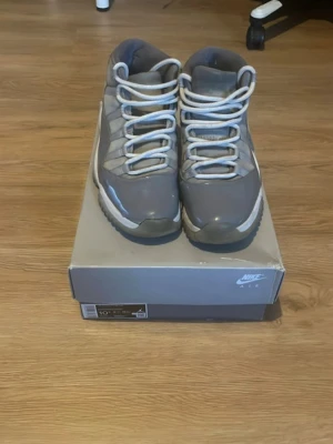 Air Jordan 11 Cool Grey sneakers - Snygga Air Jordan 11 Cool Grey sneakers med högt skaft. Skorna har en grå ovandel i läder och mesh, vita skosnören och en vit/grå sula. Ikoniska Jumpman-loggan på hälen. Perfekta för dig som gillar klassiska och stilrena sneakers.