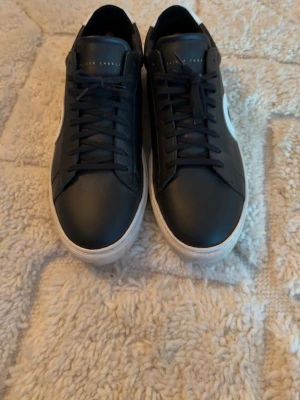 Svarta sneakers från Oliver Cabell - Snygga svarta sneakers från Oliver Cabell med vit sula och vit detalj med svart cirkel på sidan. Skorna har lågt skaft, svarta skosnören och en stilren design. Tillverkade i slätt läder med vit hälkappa och diskret logga på plösen.