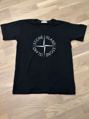 Svart Stone Island t-shirt - Snygg svart t-shirt från Stone Island med stort logotryck på bröstet. Klassisk rund hals och korta ärmar. Storlek medium och i bra skick. Skriv vid funderingar!