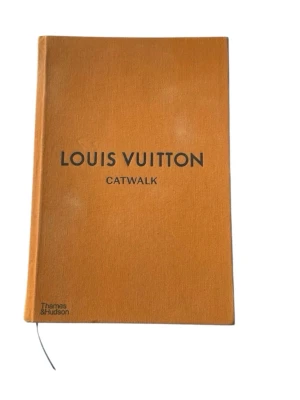 Louis Vuitton Catwalk bok - Stilren och tjock bok med orange tygklädd hårdpärm och svart text på omslaget. Boken heter 'Louis Vuitton Catwalk' och är utgiven av Thames & Hudson.  Nypris 830 kr hos louisvuitton.com! Fint skick på insidan, utsidan är sliten, texten på ryggen har färgat av sig lite. Kolla bilder noga innan köp!
