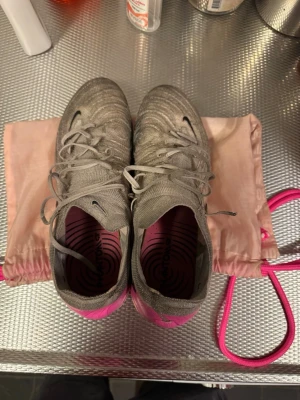 Nike Phantom GX 2 Elite - Säljer ett par Nike Phantom gx 2 elite ag för spel på konstgräs. Smutsiga men annars i bra skick. Höger skosnöre lite kortare pga har gått sönder längst upp. Annars i väl fungerande skick. Påse och box finns kvar. Kontakta gärna om ni har fler frågor!!