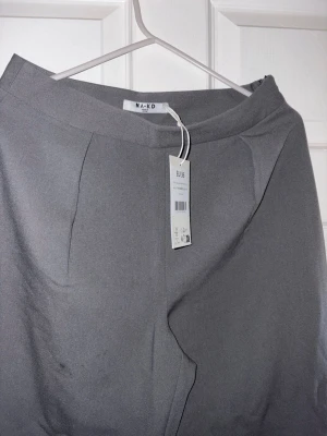 Grå kostymbyxor från NA-KD - Snygga grå kostymbyxor från NA-KD med rak passform . Byxorna har diskreta pressveck framtill och är tillverkade i ett mjukt, vävt material som ger en clean look. Helt nya, oanvända köpta i fel storlek 