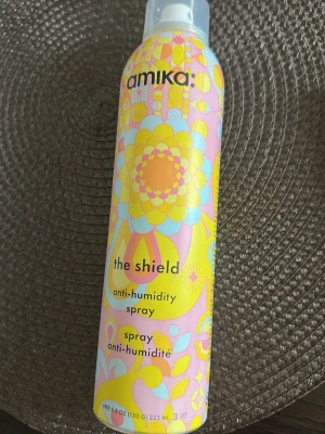 Amika The Shield anti-humidity spray - Amika The Shield anti-humidity spray i en färgglad flaska med mönster i gult, rosa, blått och vitt. Sprayen skyddar håret mot fukt och hjälper till att bevara stylingen längre. Perfekt för dig som vill ha ett frissfritt resultat. Har använt få gånger, den är som ny. 