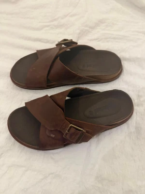 Exklusiva Timberland Bruna Sandaler Storlek 41.5 - Ett par bruna sandaler från Timberland med korsade remmar och spänne i storlek 41.5. Sandalerna har en bekväm sula och en robust design.