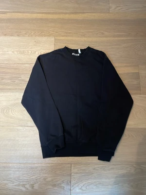 Svart sweatshirt från Weekday - En stilren svart sweatshirt från Weekday i mjuk bomull. Tröjan har rund halsringning, ribbade muddar vid ärmslut och nederkant samt en relaxed fit. Perfekt för en clean och enkel look.
