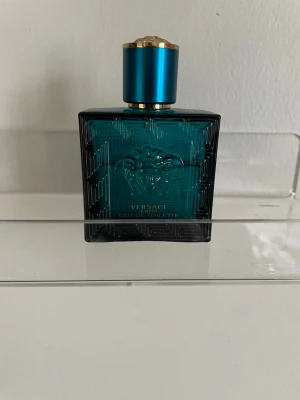 Versace Eros Eau de Toilette - Versace Eros Eau de Toilette i en stilren, fyrkantig flaska i turkost glas med elegant mönster och Medusa-huvudet på framsidan. Flaskan har ett blått och guldfärgat lock som ger en lyxig känsla. Perfekt för dig som gillar exklusiva dofter och snygg design. Lite mer en hälften kvar 