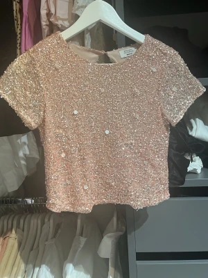 Glittrig rosa croppad topp Zara - Superfin croppad topp från Zara i ljusrosa med massor av paljetter och pärlor. Kortärmad modell med rund halsringning och glittrig yta som verkligen sticker ut. Perfekt för dig som vill ha något extra till outfiten!