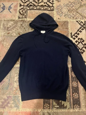 Mörkblå hoodie från Soft Goat - Säljer en mörkblå hoodie från Soft Goat i mjuk och lyxig kashmir. Hoodien har dragsko i huvan och ribbade muddar vid ärmslut och nederkant. Perfekt för dig som vill ha en stilren och bekväm hoodie med premiumkänsla. ‼️Har lagats med mocka pathes på armbågarna, och har flera andra lagningar (skickar fler bilder om du frågar)‼️