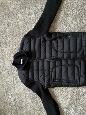 Svart quiltad cardigan från Moncler - Snygg svart cardiganjacka från Moncler med quiltad front och stickade ärmar samt rygg. Jackan har dragkedja framtill och två dragkedjeförsedda fickor. Klassisk Moncler-logga på ärmen. Perfekt för lager-på-lager och perfekt nu när det börjar bli varmare hör av dig om du har några frågar samt fler bilder😁