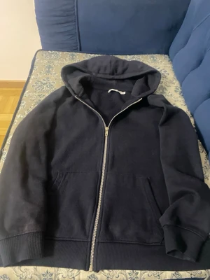 Mörk blå zip hoodie med huva - En klassisk svart hoodie med dragkedja framtill och stor huva. Hoodien har två rymliga fickor på magen och ribbade muddar vid ärmslut och nederkant. Perfekt för en avslappnad stil och enkel att matcha med det mesta. Jätte skön o fin
