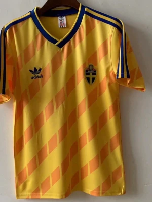 Gul Sverige retro fotbollströja Adidas - Retro Sverige fotbollströja från Adidas i gult med orangea diagonala rutor. Klassiska blå ränder på axlarna och blå detaljer vid kragen. Broderad svensk landslagssköld och Adidas-logga på bröstet. Tillverkad i lätt och ventilerande syntetmaterial. Du kan bestämma vilken storlek du vill ha!!! Tar ungefär 15-20 dagar för att tröjorna ska komma!!!