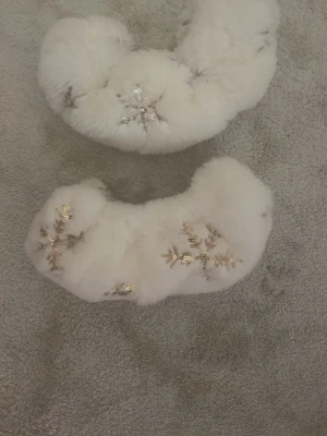 Vita fluffiga skridskor skydd - Fluffiga vita tofflor i pälsimitation med snygga guldpaljetter formade som snöflingor. Perfekta för att hålla fötterna varma och ge en mysig känsla under vintern.