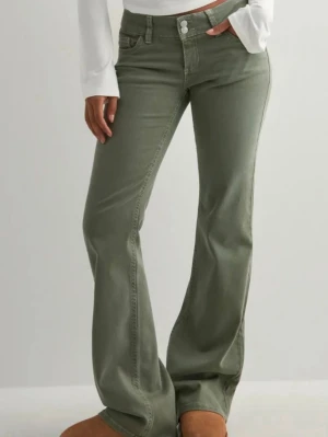 Olivgröna bootcut jeans från Wrangler - Snygga olivgröna bootcut jeans från Wrangler med klassiska fem fickor och dekorativa sömmar på bakfickorna. Jeansen har hög midja och stängs med dragkedja och två knappar. Perfekta för en avslappnad och trendig look.