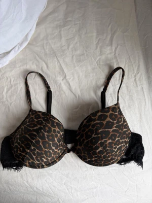 Leopardmönstrad push-up bh med spets - Snygg push-up bh med leopardmönster i brunt och svart. Axelbanden är justerbara och ryggen har svarta spetsdetaljer som ger en extra touch. Kuporna är vadderade för extra lyft och komfort. Perfekt för dig som gillar djurmönstrat och trendiga detaljer.