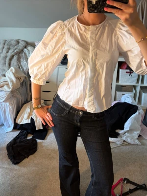 Vit blus med puffärm - Stilren vit blus med rund halsringning och puffiga trekvartsärmar. Blusen har en rak passform och knäppning framtill. Tillverkad i ett lätt bomullsliknande material som ger en fräsch och luftig känsla. Perfekt att matcha med jeans eller kjol.