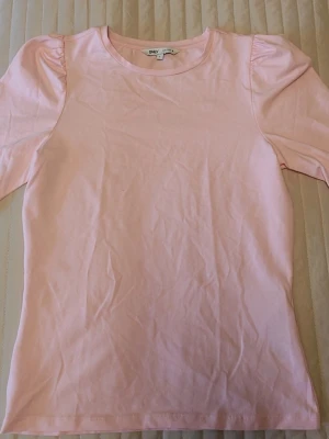 Ljusrosa topp från ONLY - Söt ljusrosa topp från ONLY med puffiga korta ärmar och rund halsringning. Tillverkad i mjuk bomull som känns skön mot huden. Enkel och stilren design som passar perfekt till jeans eller kjol.