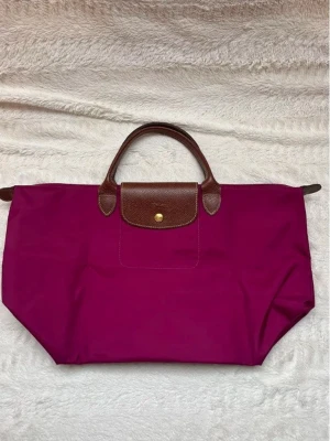 Lila Longchamp Le Pliage handväska - Stilren handväska från Longchamp i modellen Le Pliage. Väskan är cerise rosa ❤️ Storlek M 
