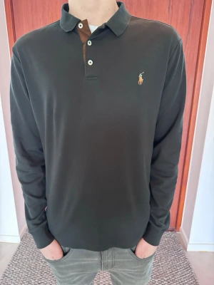Svart långärmad piké från Ralph Lauren - Snygg svart långärmad piké med den klassiska färgglada loggan. Mycket fräsch i färgen och sparsamt använd.  • Märke: Polo Ralph Lauren • Storlek: Large men sitter som Medium (Slim Fit) • Skick: Mycket bra • Färg: Svart 