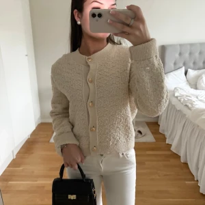 Fin kofta - Säljer en beige kofta med strukturstickat tyg och snygga guldknappar framtill. Koftan har rund halsringning, långa ärmar och ribbade muddar vid ärmslut och nederkant. Helt ny!!!! 