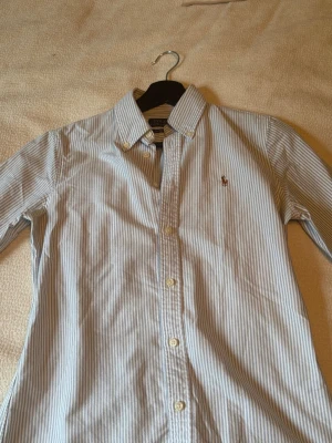 Randig skjorta från Polo Ralph Lauren - Klassisk skjorta från Polo Ralph Lauren i ljusblått och vitt med smala ränder.Tillverkad i mjuk bomull