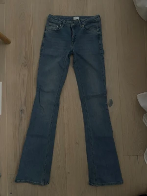 Blå bootcut jeans - Säljer ett par klassiska blå bootcut jeans och fem fickor. Jeansen har en snygg tvätt och utsvängda ben, perfekta till sneakers eller boots. Materialet är mjukt denim i bomull. Passar dig som gillar retrostil och vill ha ett par jeans som sticker ut. Sönder mellan benen men lätt att fixa.