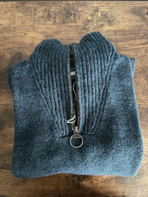 Barbour half-zipper sweatshirt - Barbour half zip stickad tröja i storlek S. Klassisk modell med hög krage, ribbad struktur och ring-zip detalj. Mörkgrå färg med diskret logga på bröstet. Väldigt clean och passar perfekt till casual/old money fits. Använd men fortfarande i bra skick, mindre tecken på användning finns.