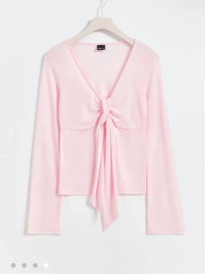 Ljusrosa långärmad topp med knyt - Trendig ljusrosa långärmad topp med djup v-ringning och knyt framtill. Toppen har en croppad passform och är tillverkad i mjukt bomullsmaterial. Perfekt för dig som gillar en feminin och stilren look.