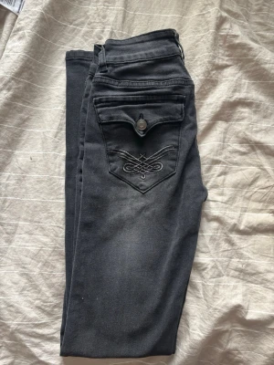 Svarta jeans från Madlady med detaljer - Säljer ett par svarta jeans från Madlady med dekorativa sömmar framtill och snygg broderad bakficka med knapp. Jeansen har hög midja, dubbla knappar och smal passform. Perfekta för dig som gillar stilrena men ändå unika detaljer. 