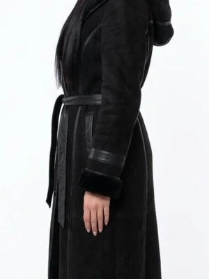 Svart lång fårskinnskappa med huva - Snygg svart lång kappa i fårskinn med huva och bälte i midjan. Kappan har detaljer i läder, breda muddar i fuskpäls och markerade sömmar. Perfekt för kalla dagar när du vill vara både varm och stilren.