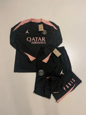 PSG tracksuit (tränings ställ) (byxor och tröja) - Säljer en riktigt snygg PSG-tränings ställ. svart med rosa detaljer, i riktigt fint skick – aldrig använd. Perfekt för dig som vill vara varm men ändå ha ett snyggt ställ. Storlek passar som S på både tröjan och byxan. Stället kommer i original förpackning. Om du har några frågor eller vill se fler bilder är de bara att skriva!🙂 Kolla gärna på mina andra artiklar, så kanske du hittar något du gillar! 