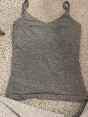 Grå ribbad linnetopp - Säljer en enkel och stilren grå linnetopp med smala axelband och ribbad struktur. Toppen har en lätt v-ringad halsringning och är perfekt för lager på lager eller till jeans. Superenkel att matcha och passar till det mesta!