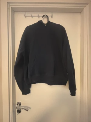 Mörkblå hoodie från 157 - En enkel och stilren mörkblå hoodie från 157 med klassisk huva och ribbade muddar. Hoodien är tillverkad i mjukt bomullsmaterial och har en avslappnad passform. Perfekt för dig som gillar en clean och bekväm look.