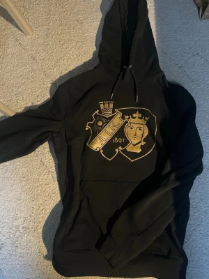 Svart AIK hoodie med guldfärgat tryck - Säljer en svart hoodie från norra stå  med stort guldfärgat . Emblem den såldes av ultras nord och denna går endast att köpa på norra och den säljs inte längre 