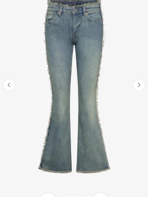 Tvåfärgade Bootcut jeans med fransar - Säljer ett par blå bootcut jeans med fransiga, råa kanter längs sidorna och i midjan. Använd ett fåtal ggr så alltså i bra skick. Köpta från monki.