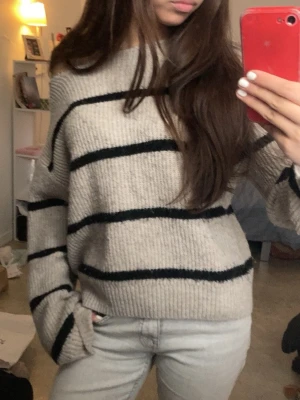 stickad off shoulder tröja  - Säljer en oversized beige stickad tröja med breda svarta horisontella ränder. Tröjan har en avslappnad passform, långa ärmar och kan bäras off-shoulder för en trendig look. Perfekt till jeans och enkel att styla. Materialet känns mjukt och mysigt. Tröjan va först en turtle neck tröja som jag har klippt till en off shoulder. Det syns Inte så mycket att den är klippt när man har på sig den. Skriv för fler bilder🤍