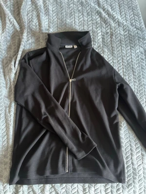 Svart ziptröja från Only & Sons - Säljer en svart långärmad ziptröja från Only & Sons. Tröjan har hög krage och dragkedja framtill som går snett över bröstet. Tillverkad i mjukt material, perfekt för en avslappnad och stilren look.